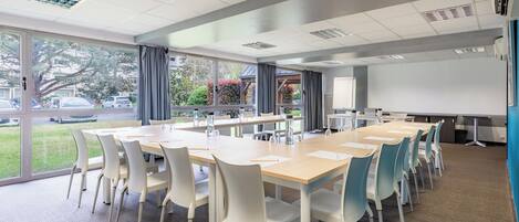 A conference room with a large table, white chairs, and a projector screen.