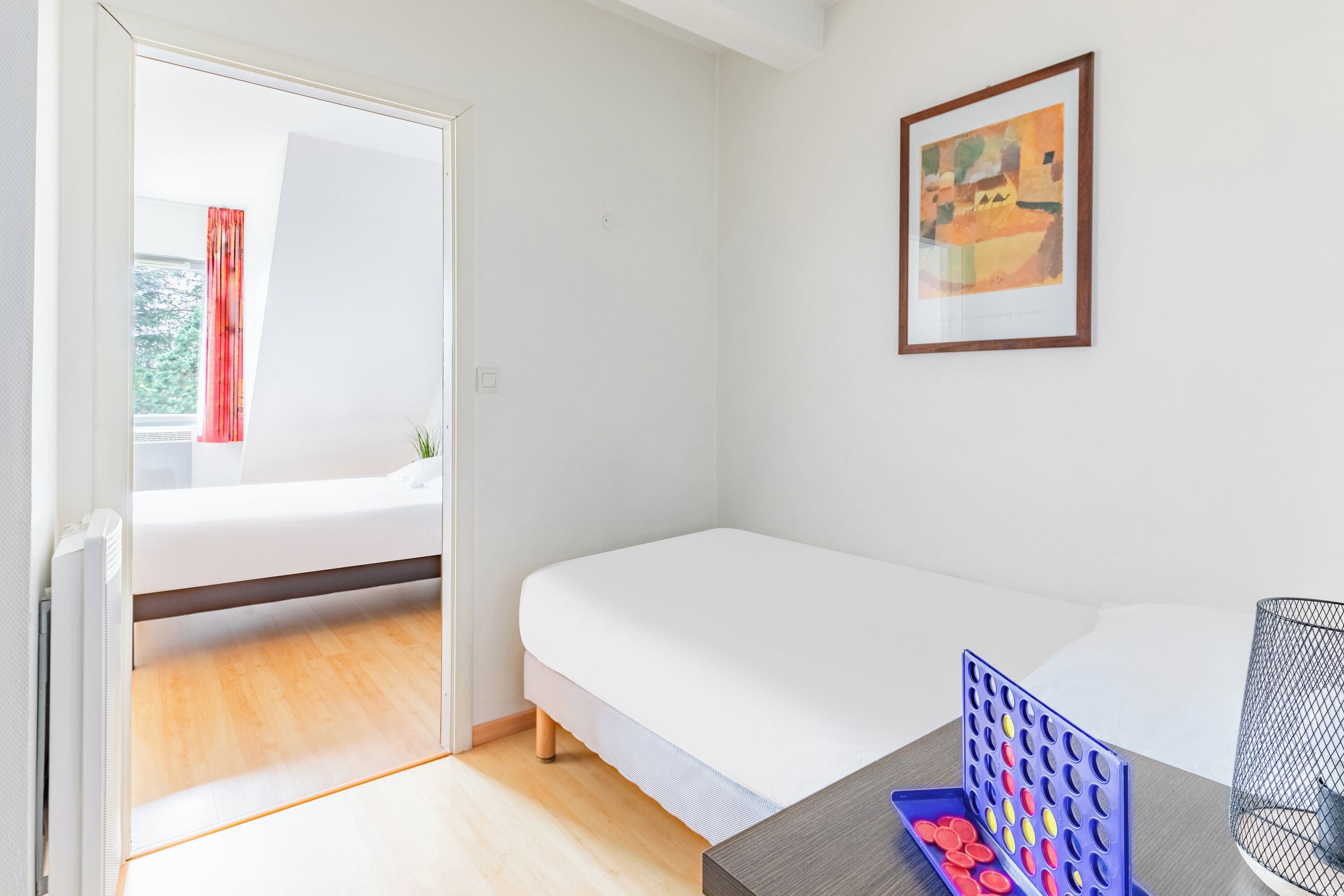 Quarto com cama, escrivaninha com um objeto azul e um quadro na parede.