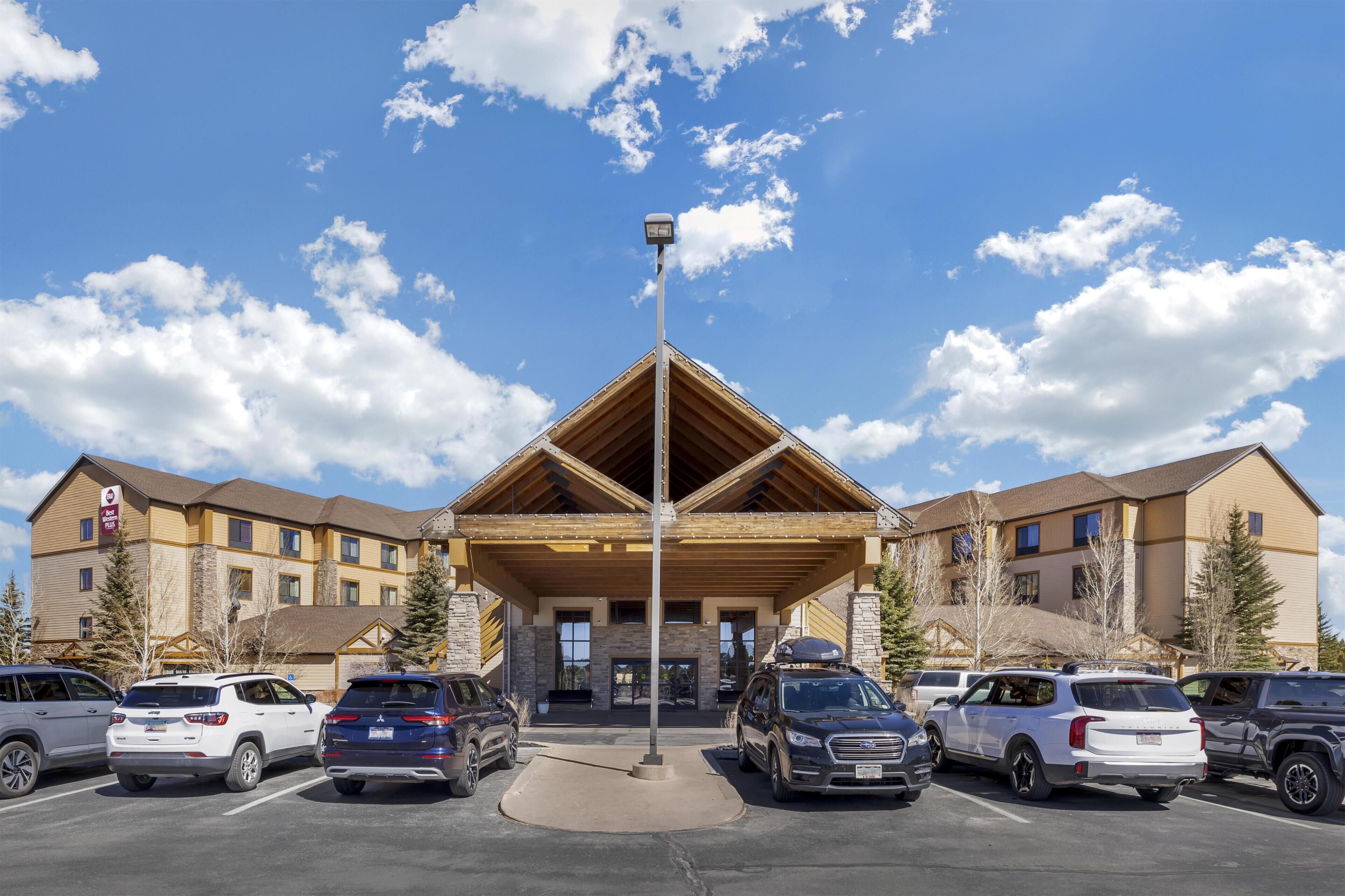 A hotel with a central entrance, multiple parking spaces, and a clear sky.