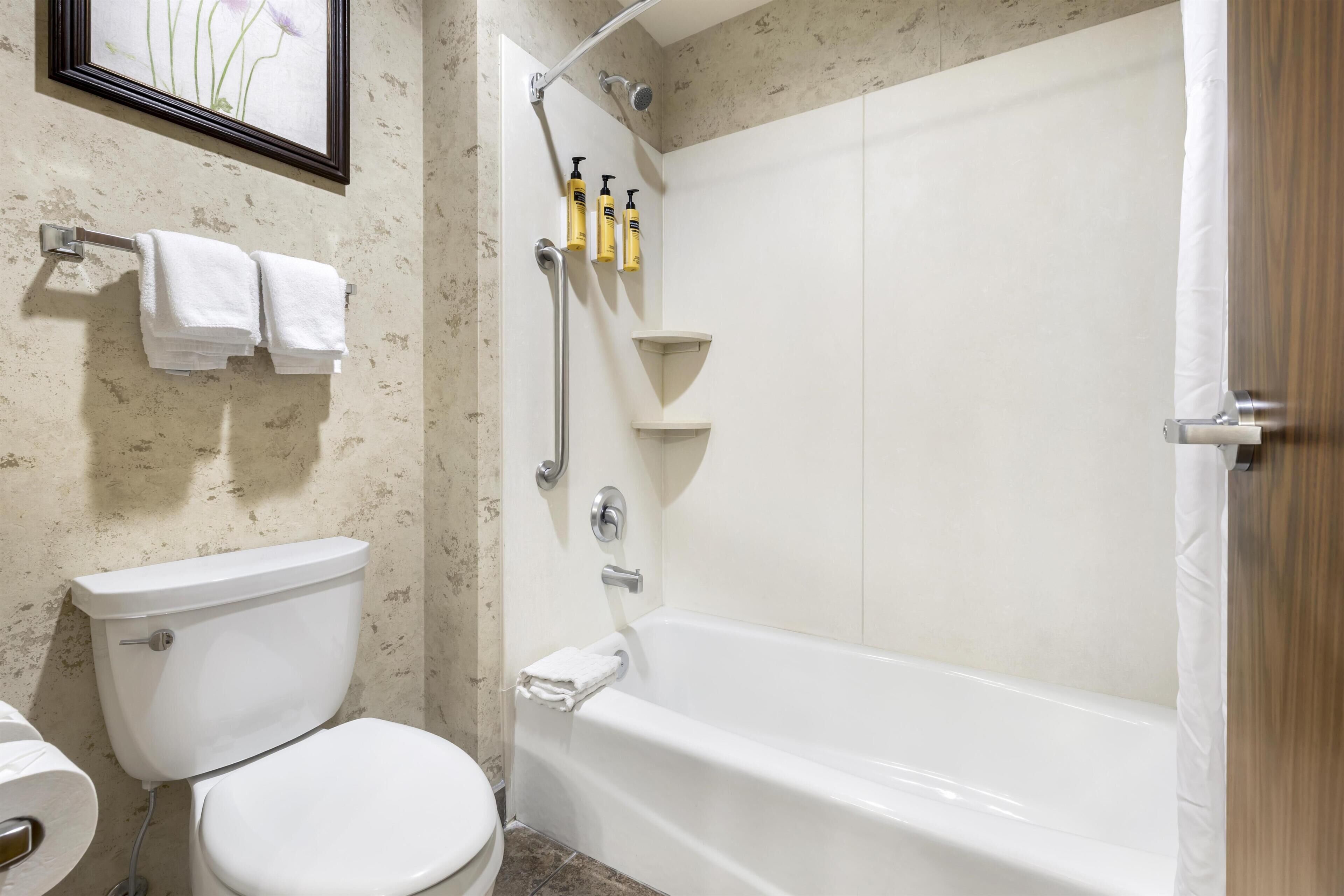 A bathroom with a toilet, a bathtub, and a shower. There are towels hanging on a rack and a framed picture on the wall.