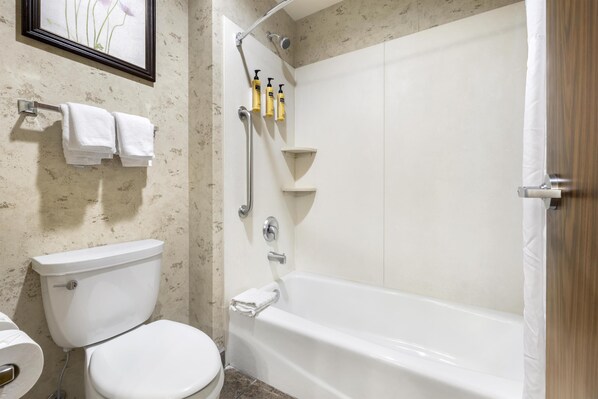 Un baño con inodoro, bañera y ducha. Hay toallas colgadas en un perchero y un cuadro en la pared.