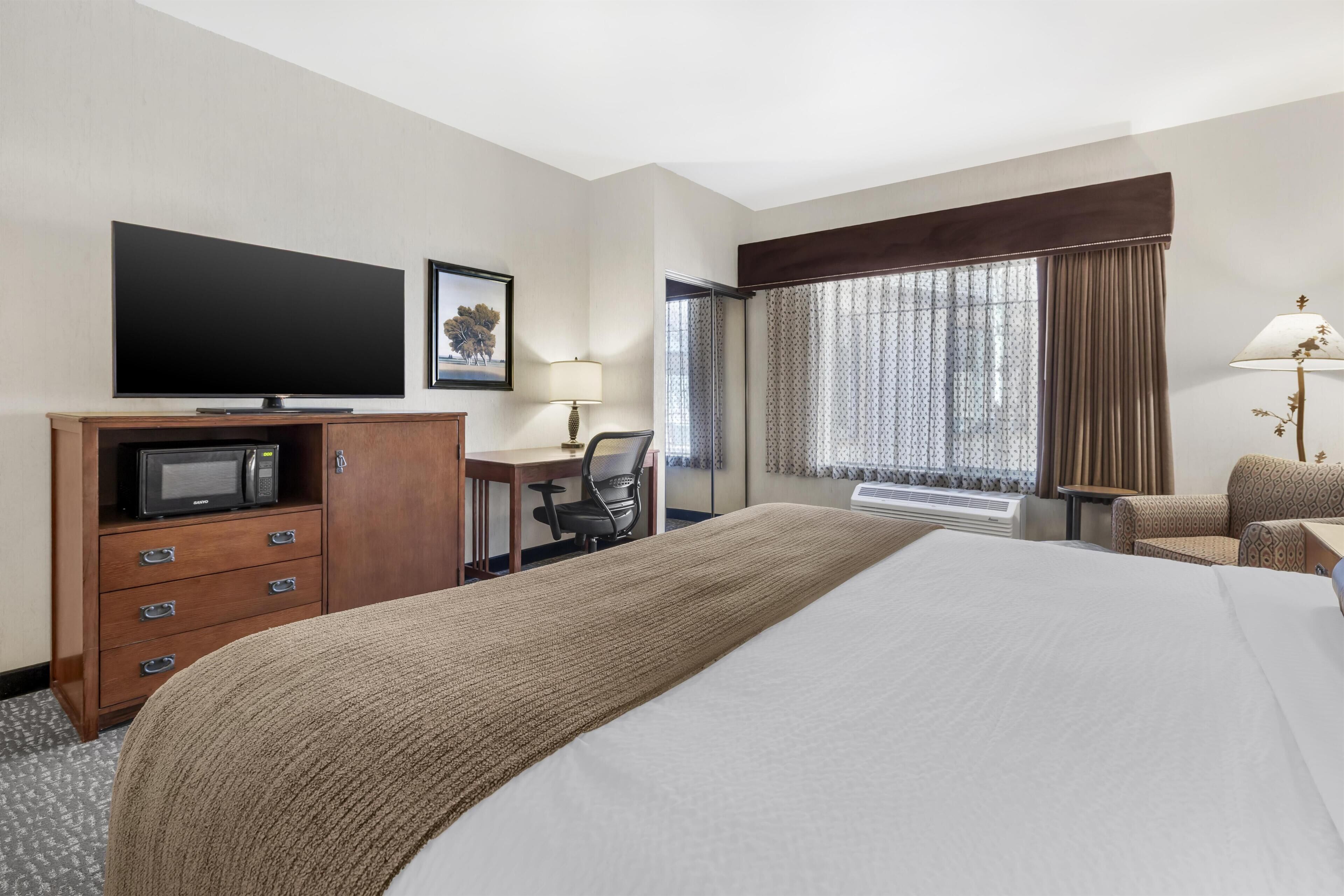 Een hotelkamer met een groot bed, een bureau met stoel, een televisie, een magnetron en een raam met gordijnen.