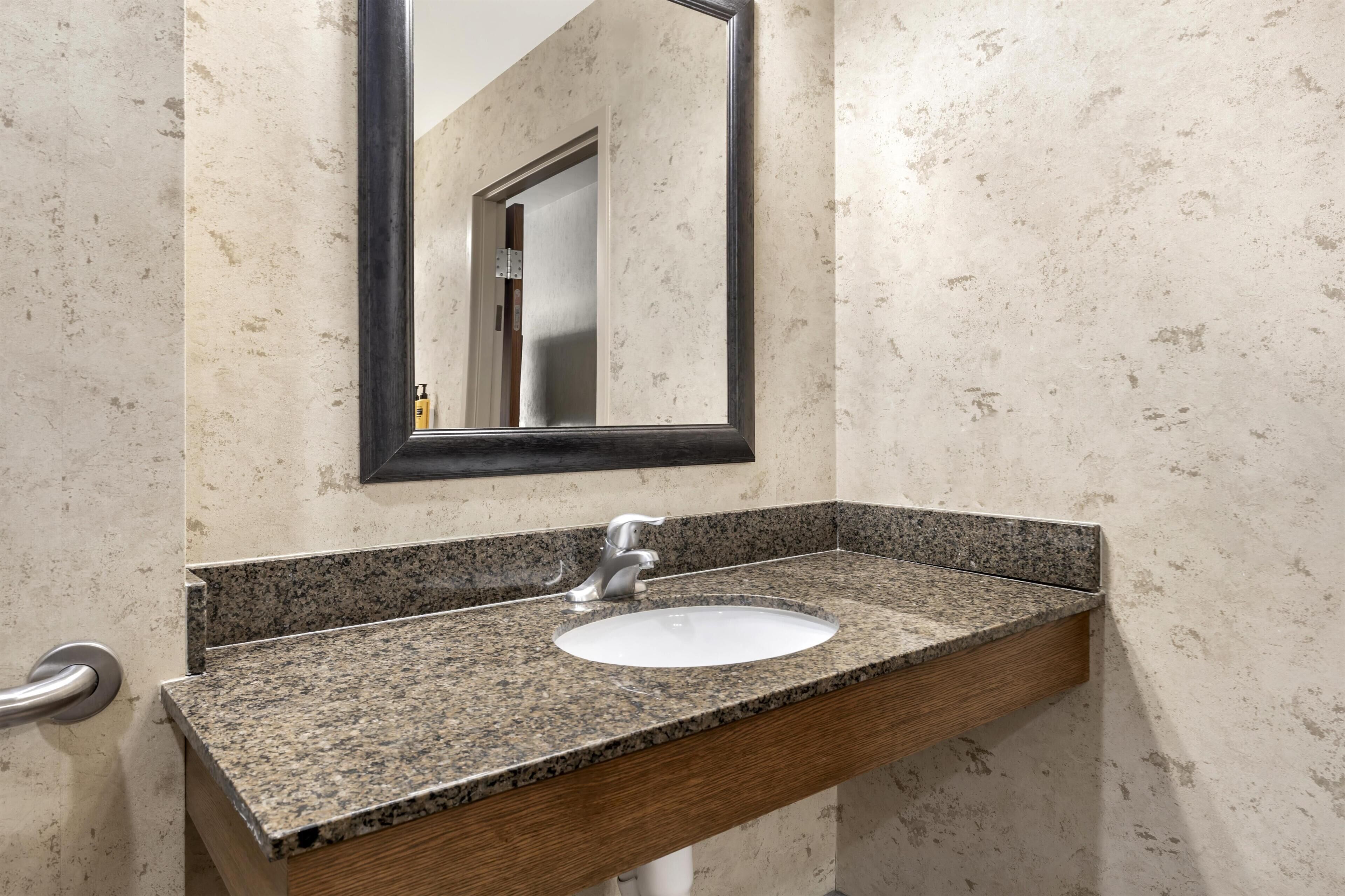 A bathroom with a granite countertop sink, a wooden vanity, and a mirror with a black frame.