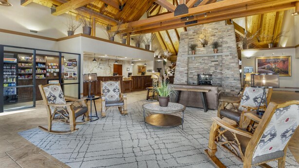 Un hall d’entrée spacieux avec des poutres en bois, une cheminée en pierre et un coin salon agrémenté de fauteuils à motifs et d’une table ronde.