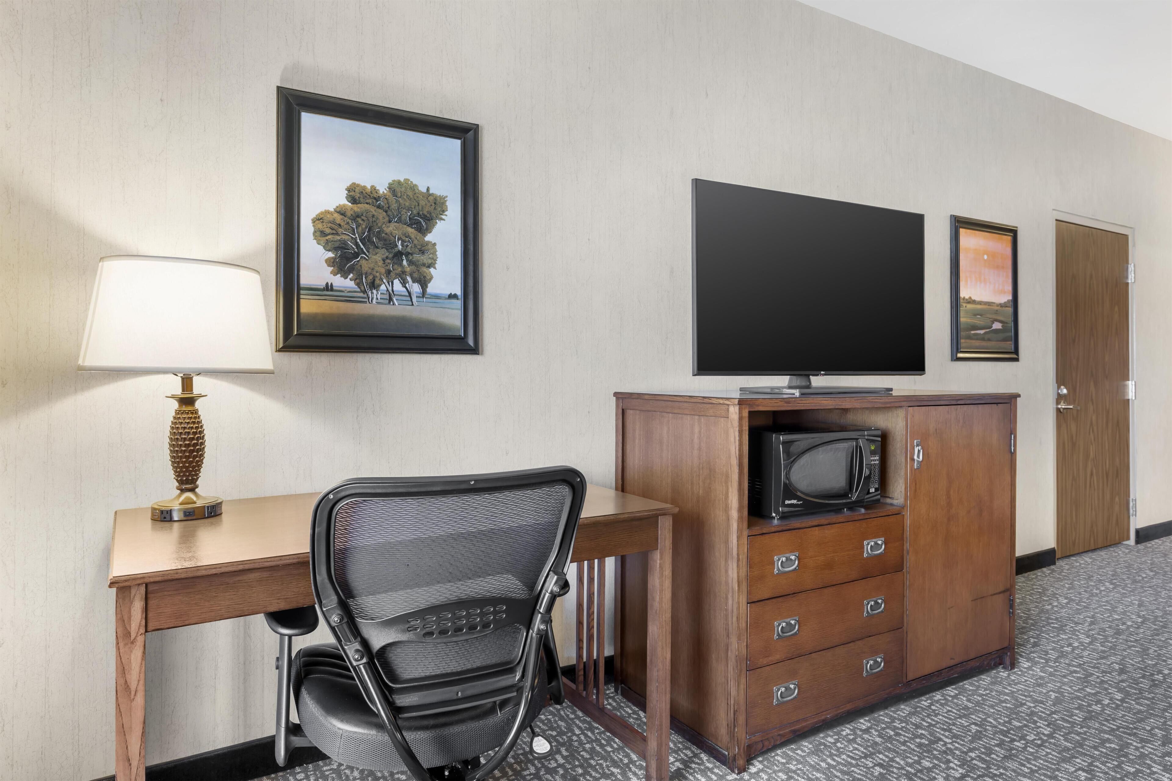 A hotel room with a desk, chair, television, microwave, and a cabinet with drawers.