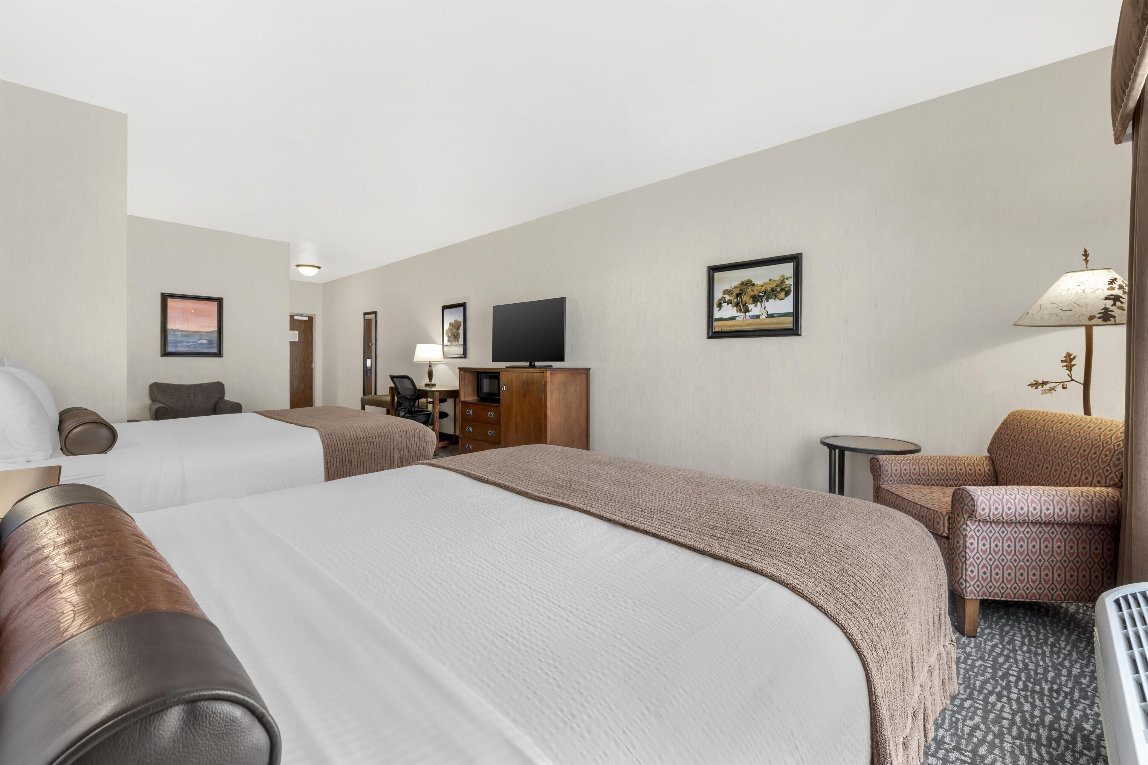 Quarto de hotel com duas camas, televisão, escrivaninha, cadeira e luminária.