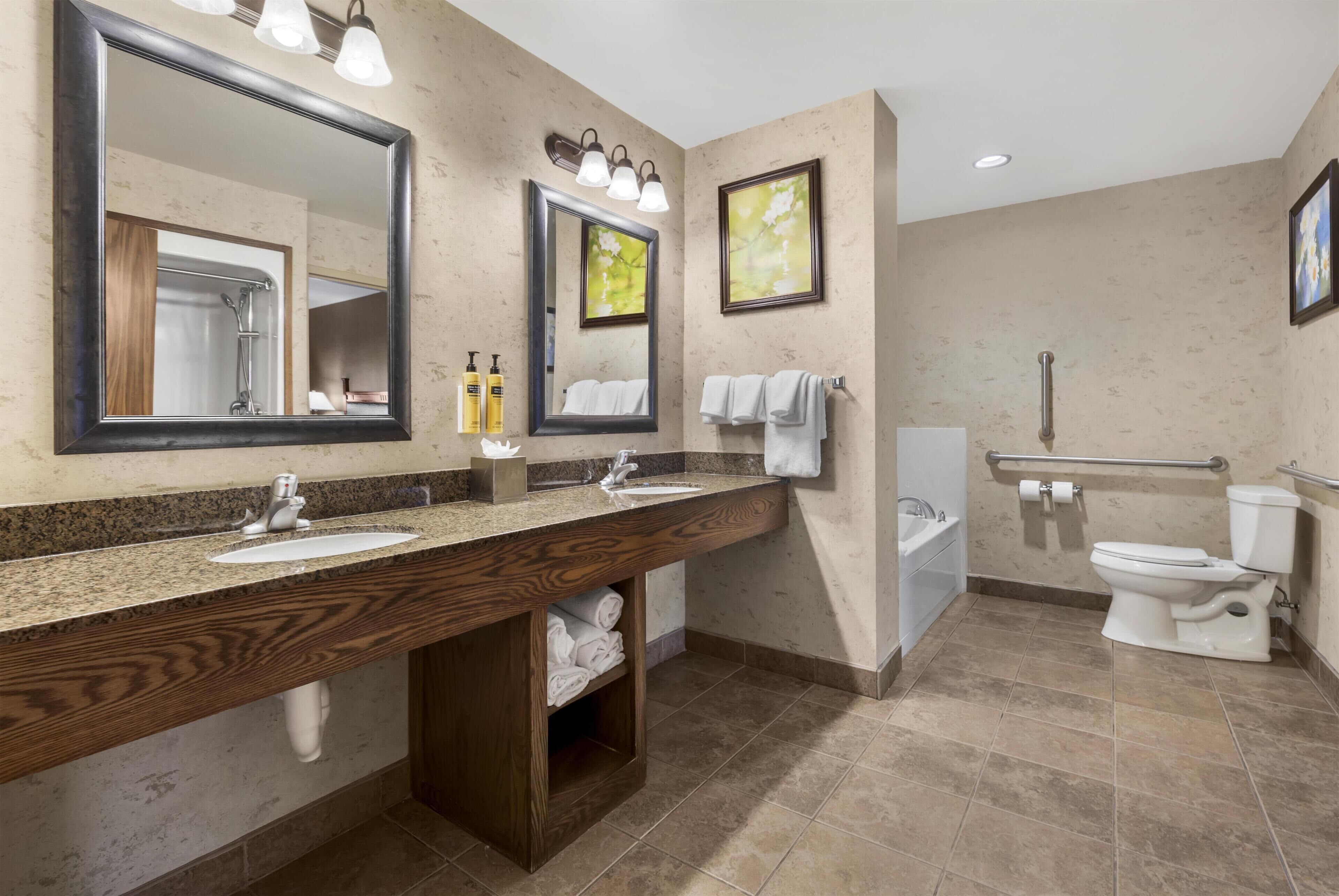 A modern bathroom with a large mirror, two sinks, a toilet, and a shower.