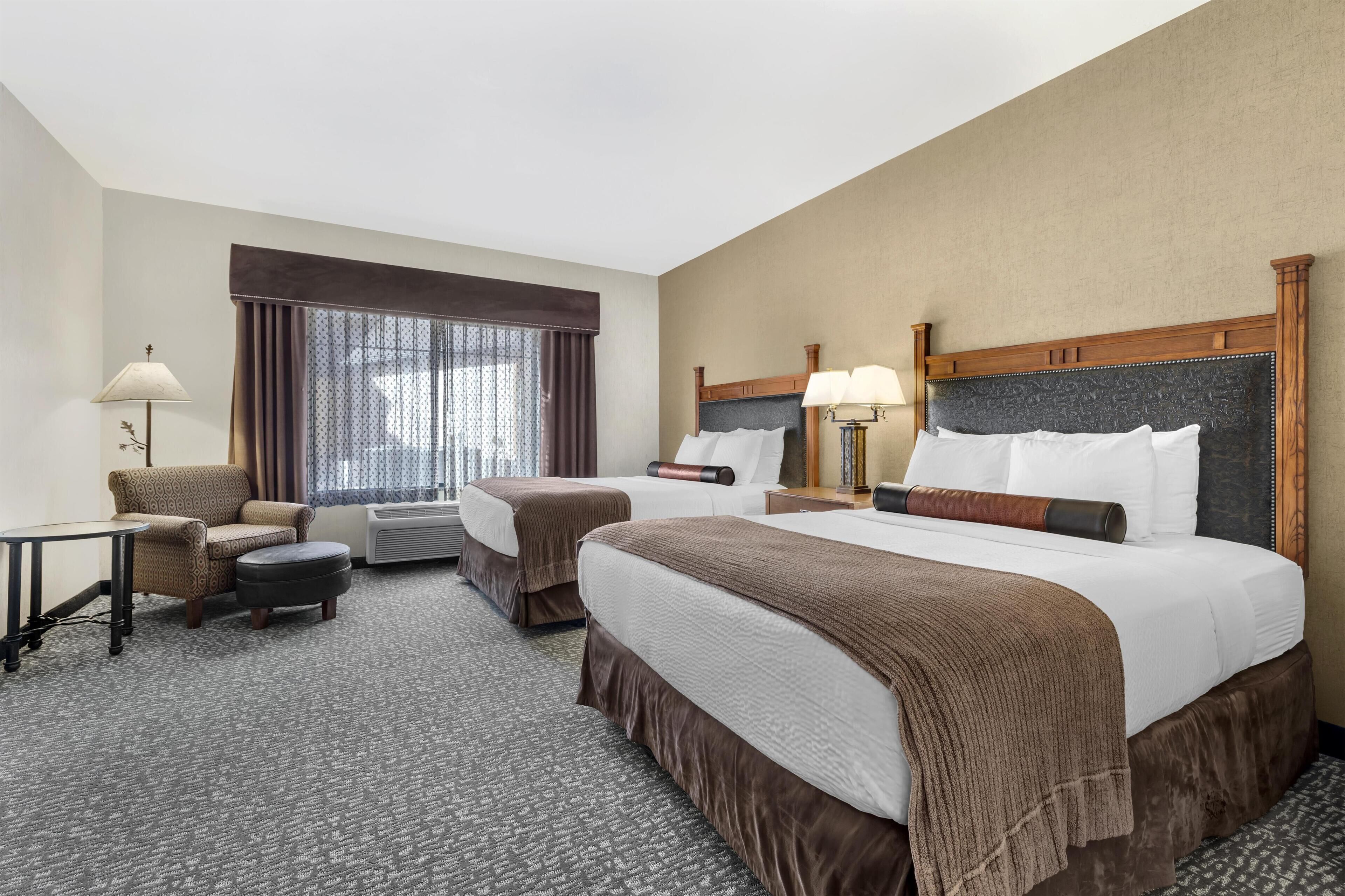 A hotel room with a large bed, a smaller bed, a sofa, a desk, and a window with curtains.