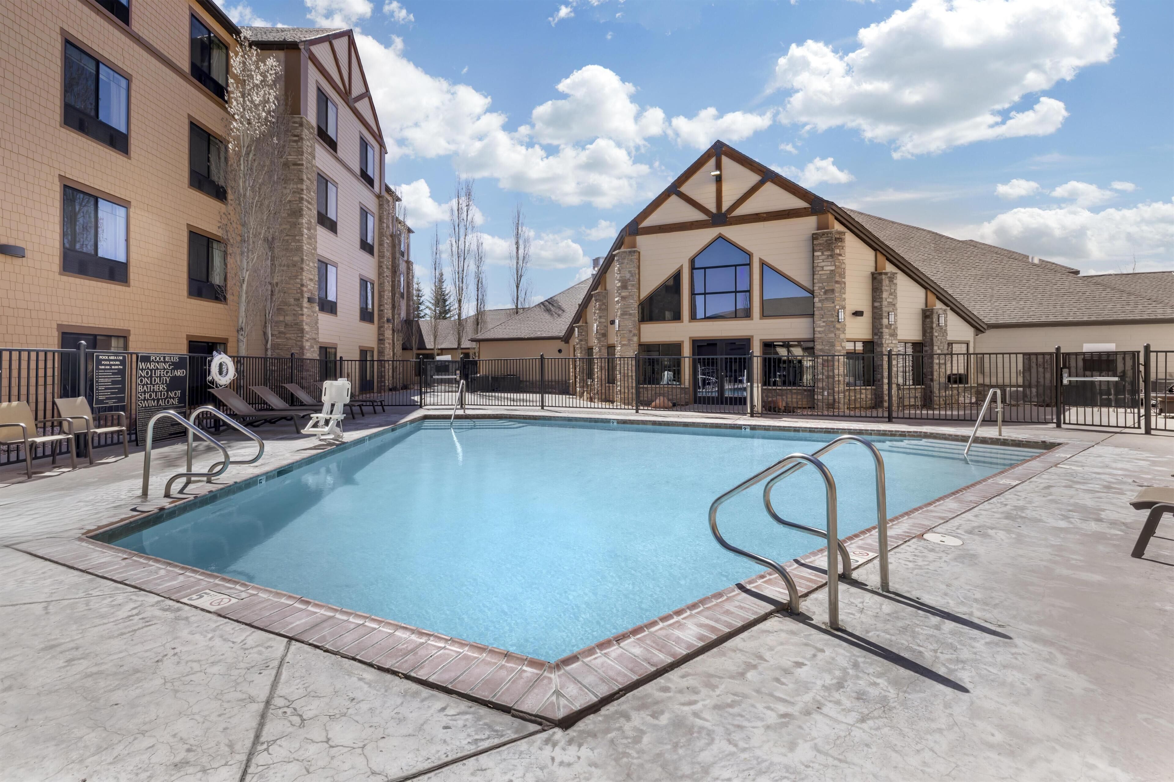 A swimming pool with a brick border, a covered area, and a building with multiple windows and a large skylight.