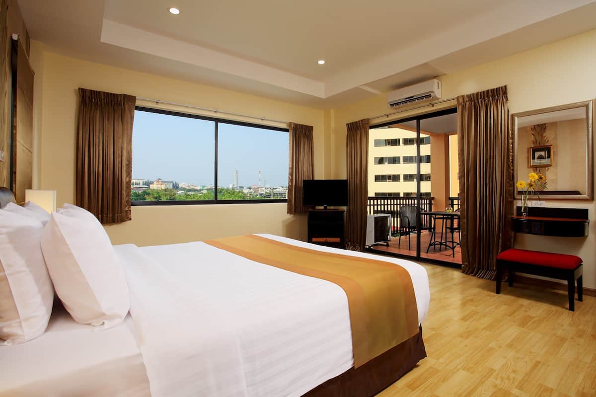 A hotel room with a large bed, a desk with a chair, a television, and a balcony with curtains.
