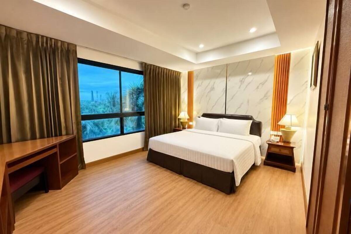A hotel room with a bed, bedside tables, a desk, a window with curtains, and a view of the outdoors.