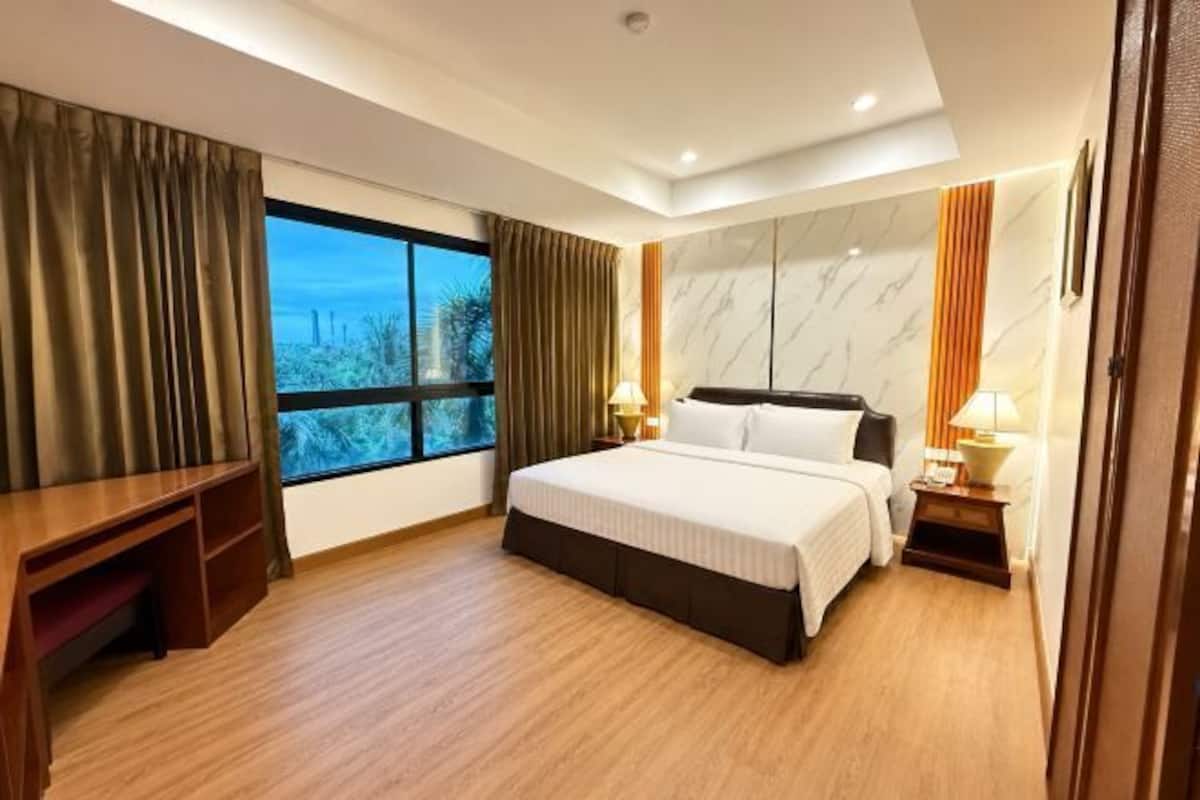 Quarto de hotel com cama, mesas de cabeceira, escrivaninha, janela com cortinas e vista para o exterior.
