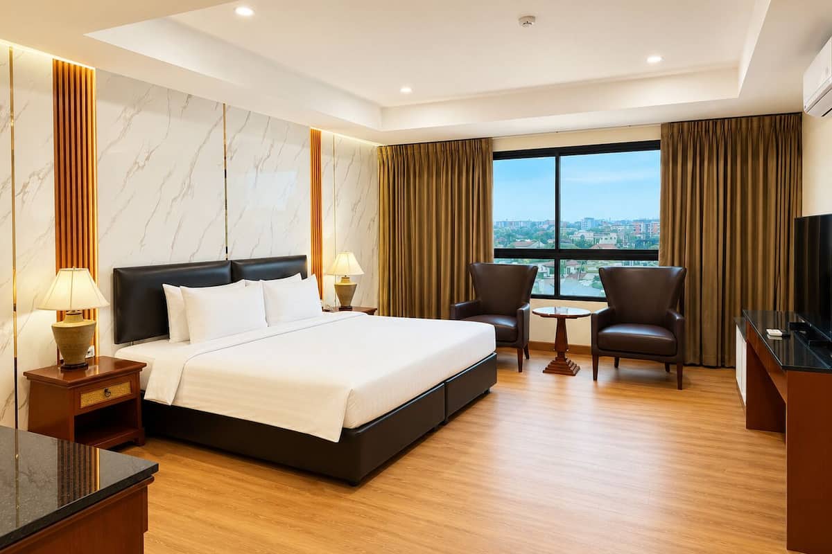 A hotel room with a bed, two chairs, a small table, a TV, and a city view.