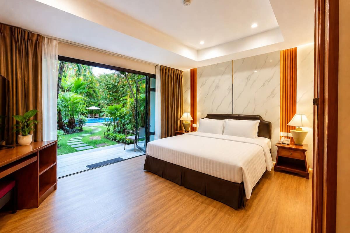 A modern hotel room with a large bed, a TV, a desk, and a view of a lush garden.