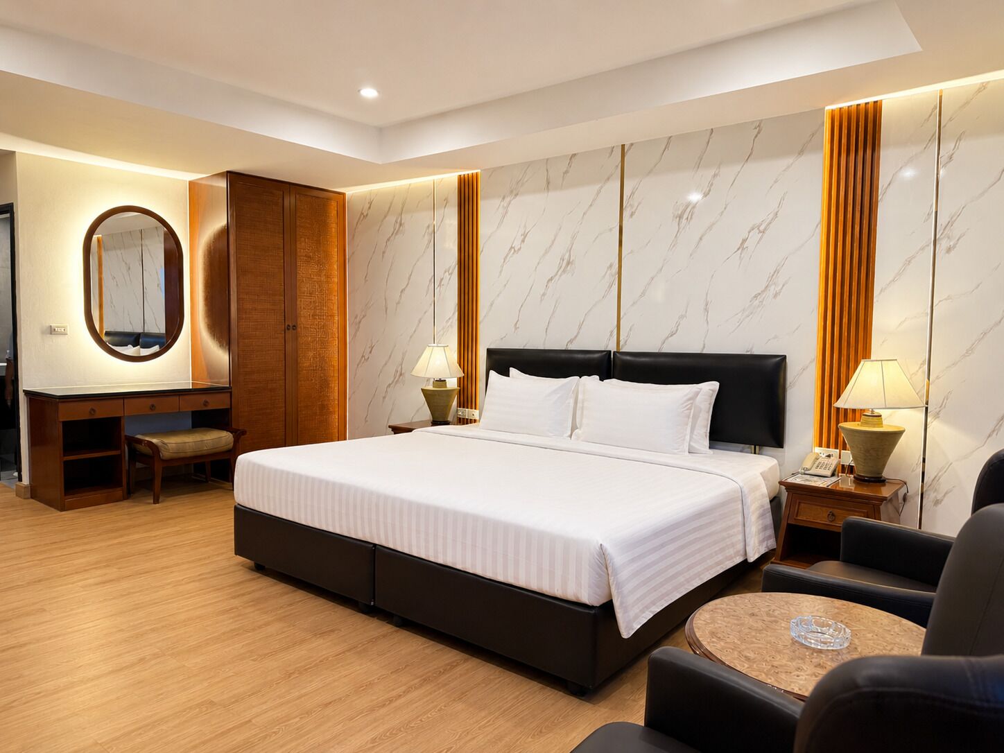 A hotel room with a large bed, a desk with a chair, a round coffee table, and a mirror.