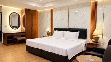 A hotel room with a large bed, a desk with a chair, a round coffee table, and a mirror.
