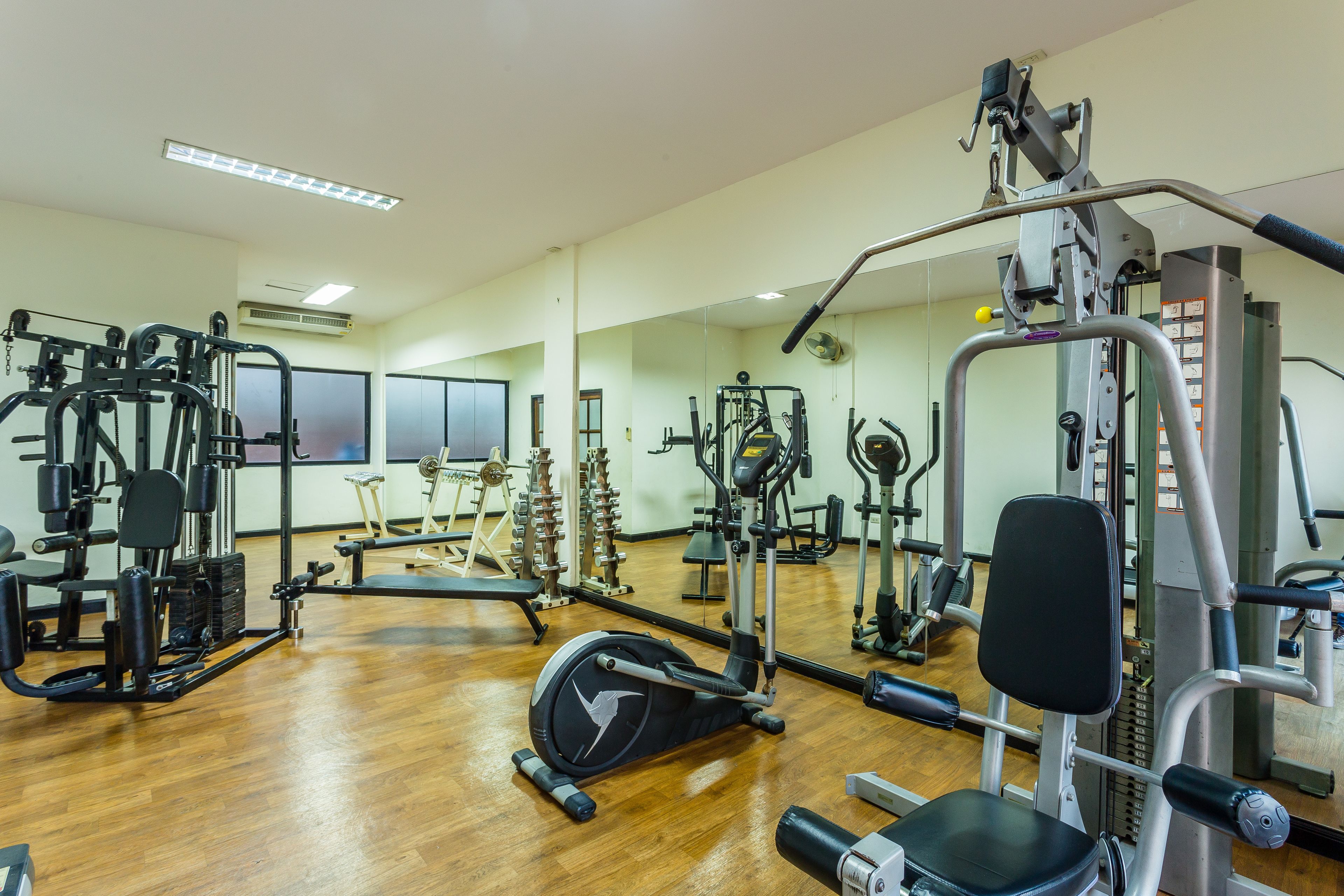 A gym with various exercise equipment, wooden flooring, and a mirror.