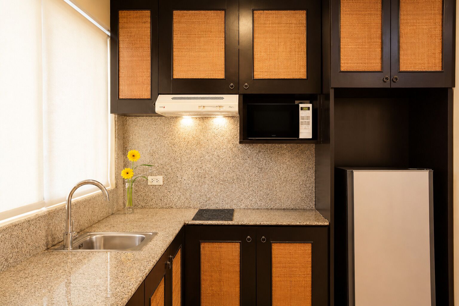 A kitchen with granite countertops, a stainless steel sink, a microwave, and a refrigerator.