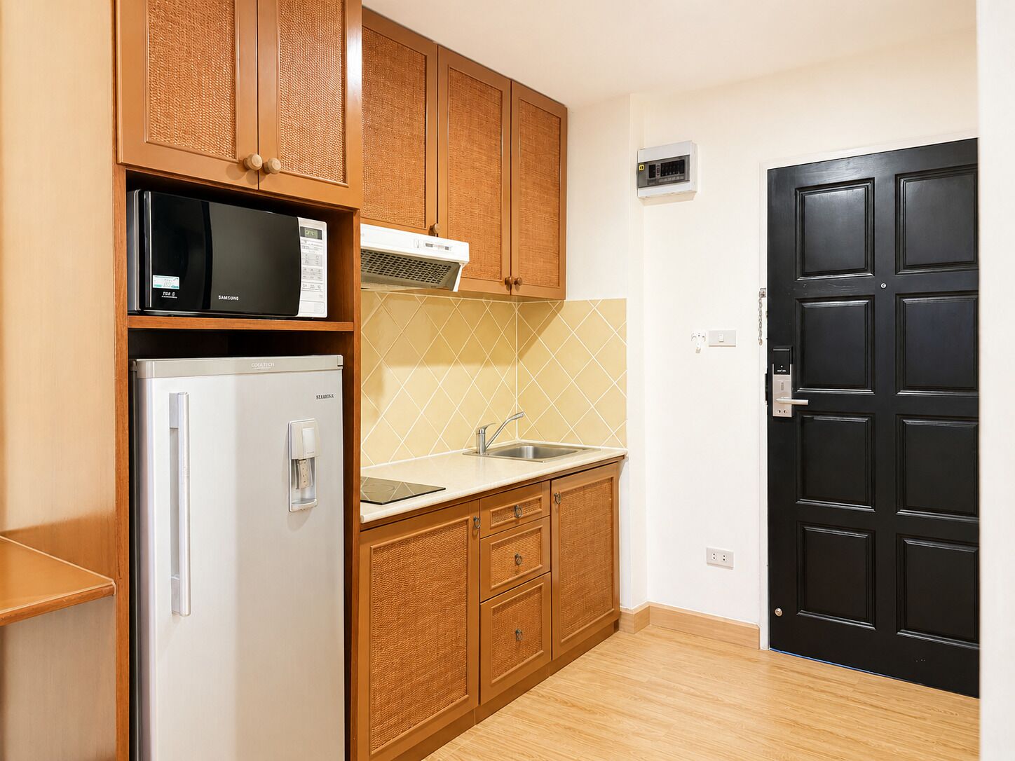 A compact kitchen with a refrigerator, microwave, and stove, wooden cabinets, a sink, and a black door.