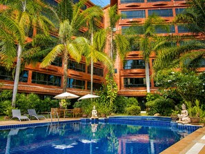 Un hotel con piscina rodeada de palmeras y una estatua de Buda.