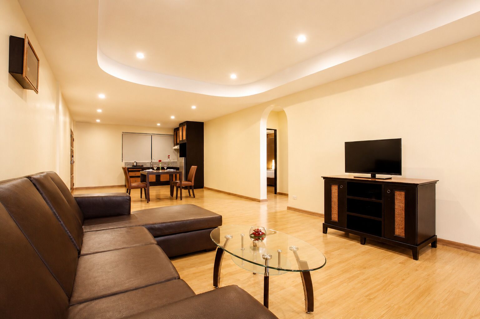 A modern living room with a sectional sofa, a glass coffee table, and a flat-screen TV on a cabinet.