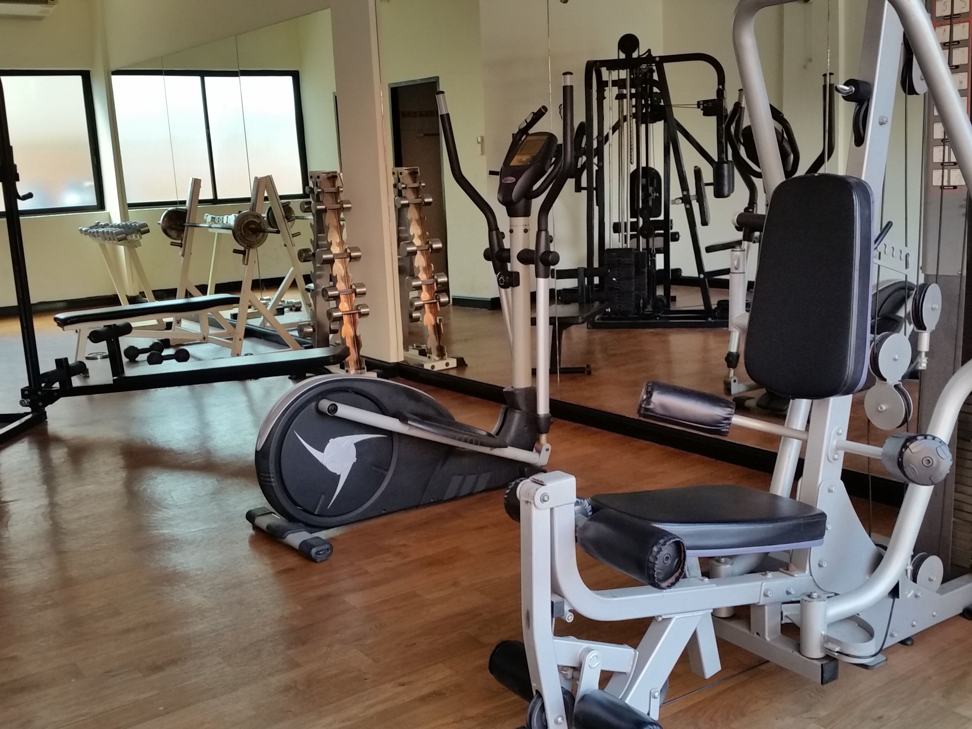 A gym with various exercise equipment, including a treadmill, weight machines, and a mirror reflecting the space.