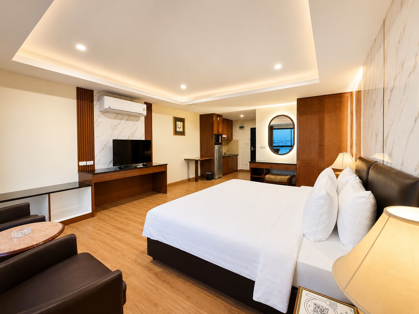 Habitación de hotel con cama, escritorio, televisión, una pequeña kitchenette y vista a la ciudad.