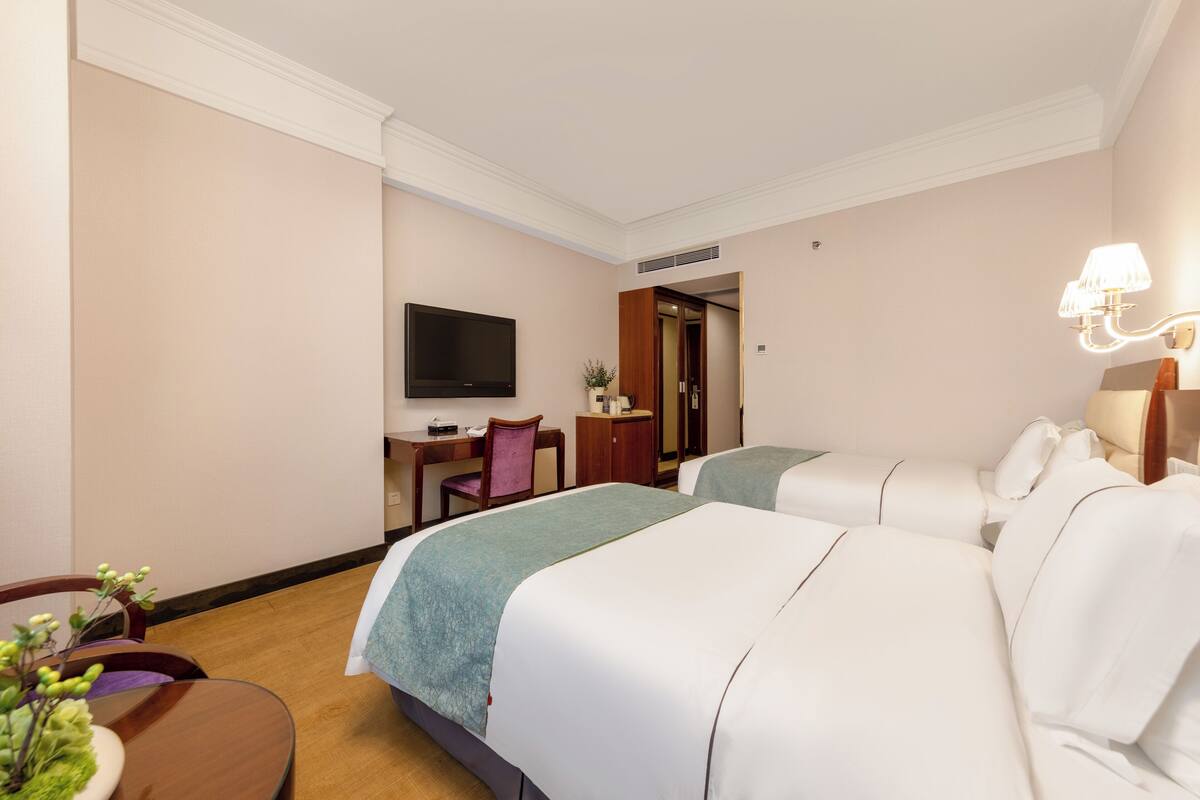 A hotel room with two beds, a desk, a chair, a television, and a lamp.