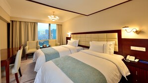 A hotel room with two beds, a desk, a chair, and a view of the city.