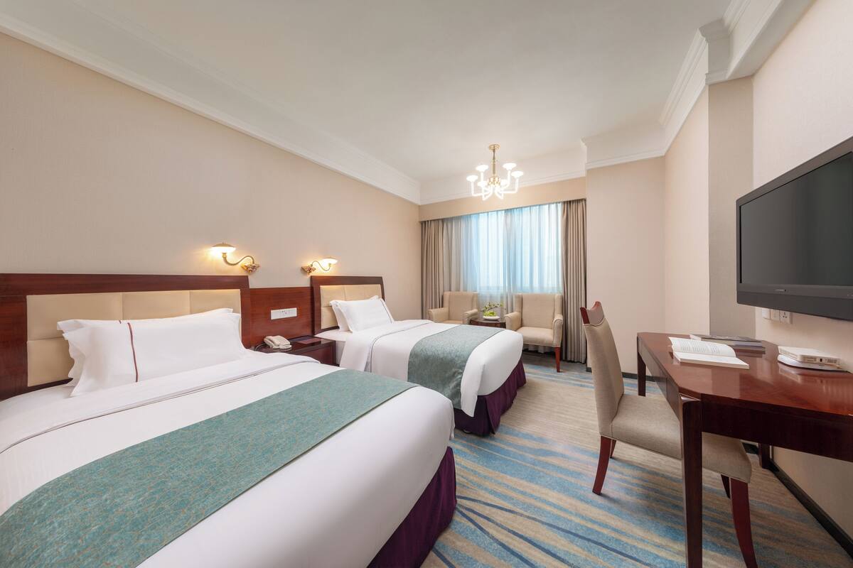 A hotel room with two beds, a desk, a chair, a television, and a window with curtains.