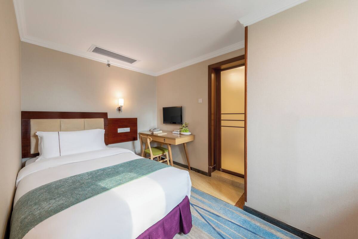 A hotel room with a bed, desk, chair, TV, and a door leading to another room.