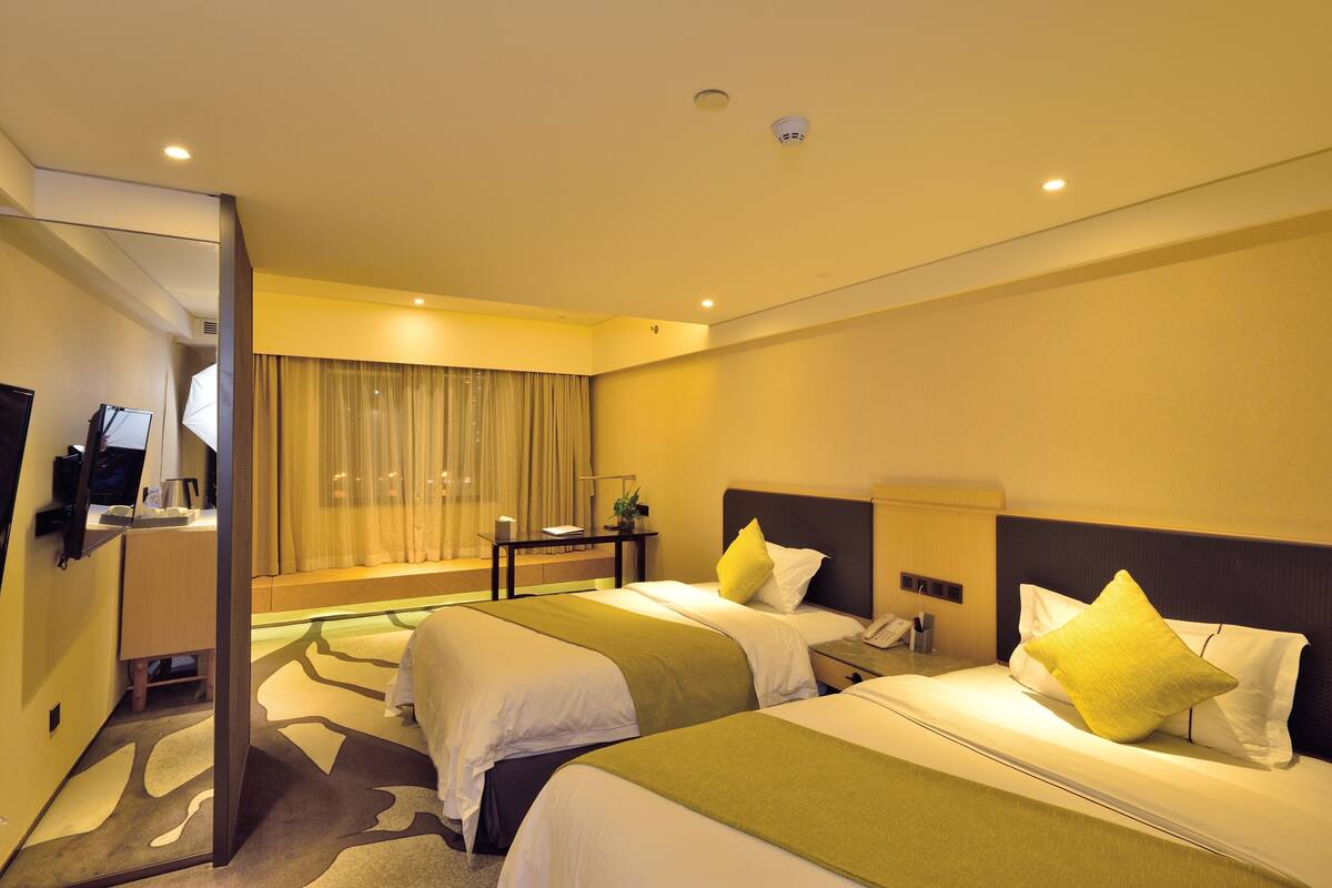 A hotel room with two beds, a desk, a chair, a mirror, and a window with curtains.