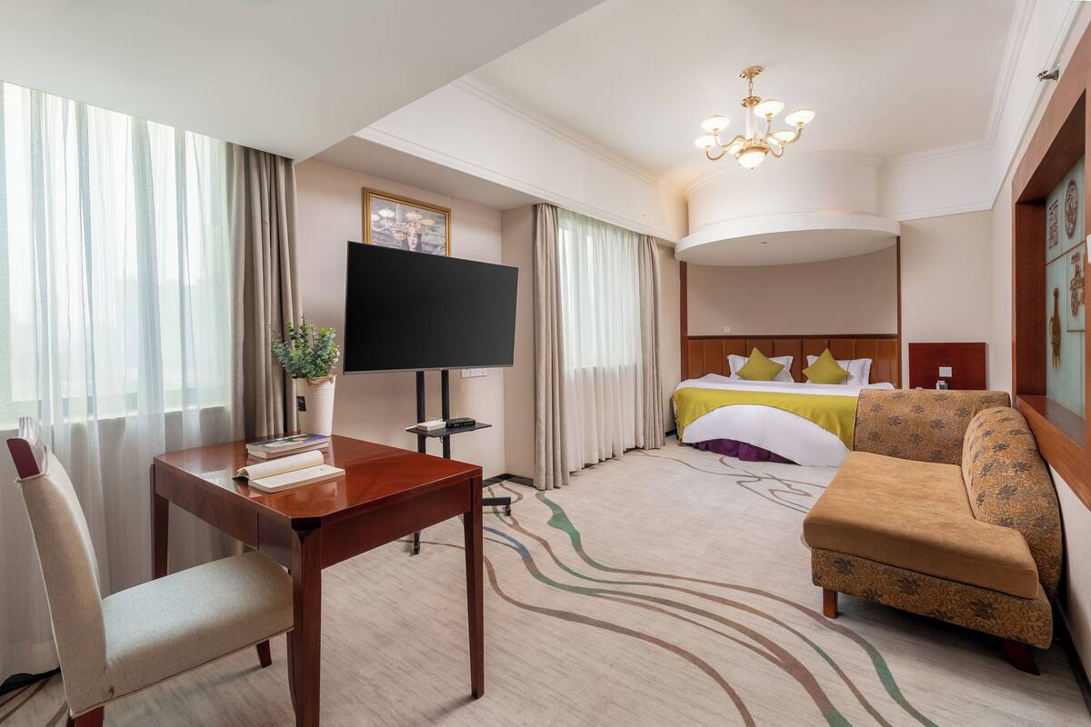 A hotel room with a bed, a TV, a desk, a chair, and a sofa.