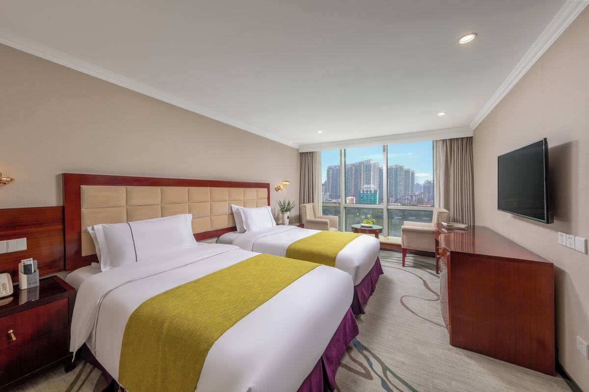 A hotel room with two beds, a desk, a TV, and a city view.