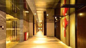 A corridor with a marble floor, glass elevator doors, and a red decorative element on the wall.