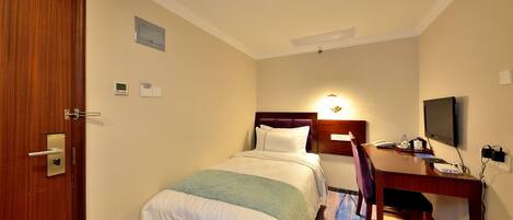 A hotel room with a bed, a desk with a chair, a television, and a trash bin.