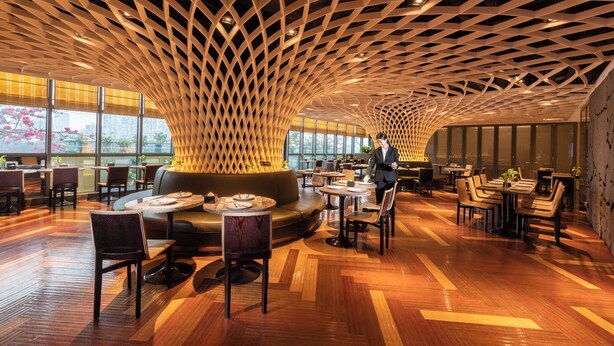 A modern restaurant with a unique lattice ceiling, wooden flooring, and a mix of seating arrangements including tables and a sofa.