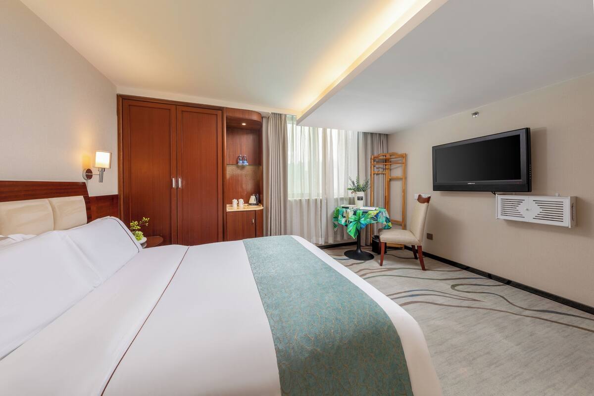 A hotel room with a large bed, a desk with a chair, a television, and a wardrobe.
