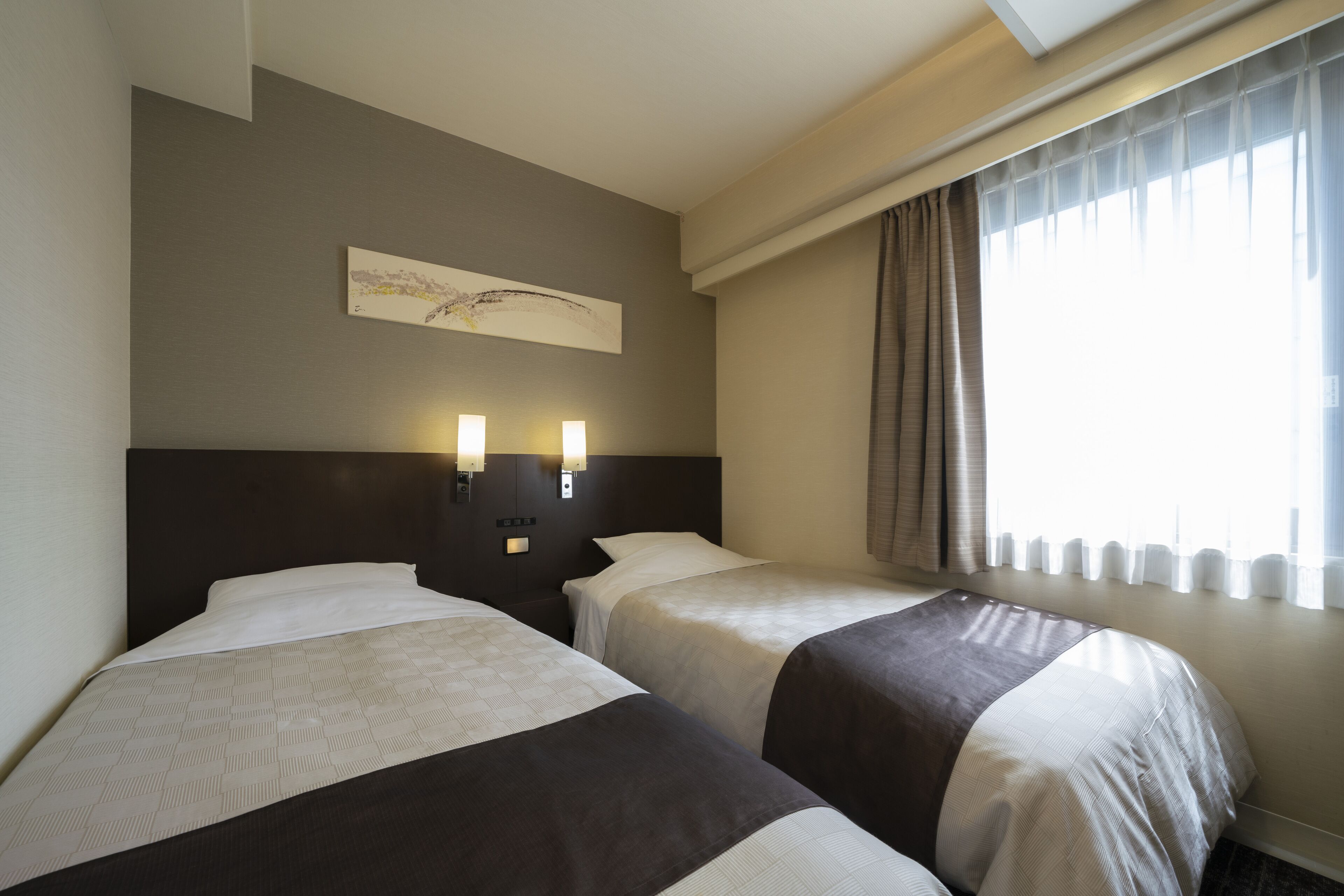 A hotel room with two beds, a headboard with wall-mounted lights, a window with curtains, and a painting on the wall.