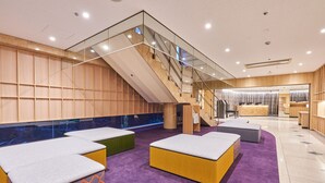 Un moderno vestíbulo de hotel con alfombra púrpura, zonas de estar, una escalera y paneles de madera.