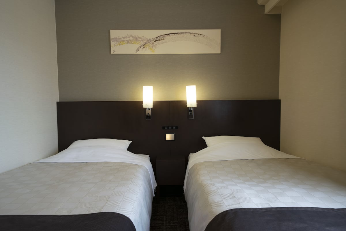 Une chambre d’hôtel avec deux lits simples, une tête de lit dotée de lampes murales et une petite table placée entre les lits.