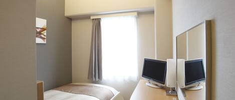 A hotel room with a bed, a desk with two monitors, a telephone, and a window with curtains.