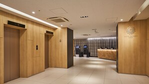 Un vestíbulo de hotel con paneles de madera, un mostrador de recepción y un quiosco digital de registro.