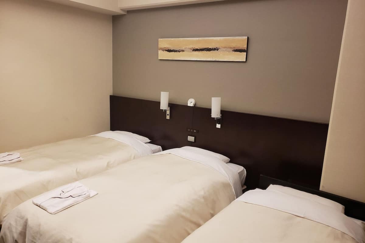 Une chambre d’hôtel avec deux lits simples, une tête de lit, une horloge murale et un tableau.