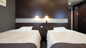 Habitación de hotel con dos camas individuales, cabecera oscura, lámparas de noche y una mesita de noche.