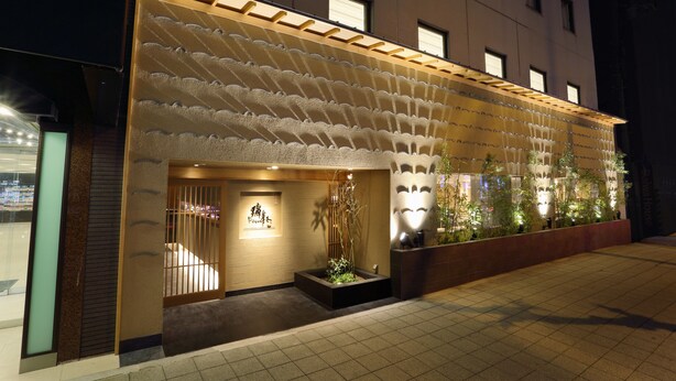 Entrada de hotel con fachada moderna, una zona de recepción y un pequeño jardín con plantas.