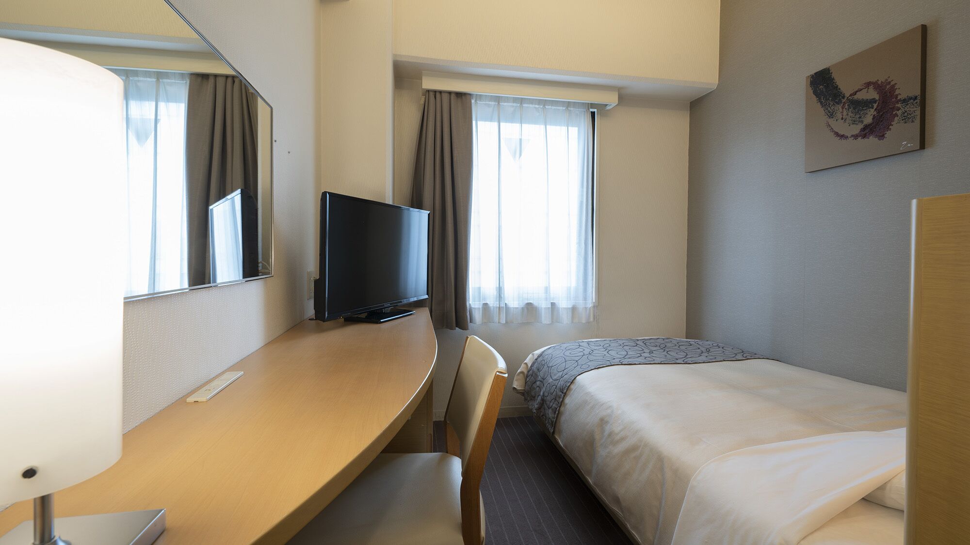 Ein Hotelzimmer mit Bett, Schreibtisch, Sessel, Fernseher und einem fensterbepflanzten Fenster.