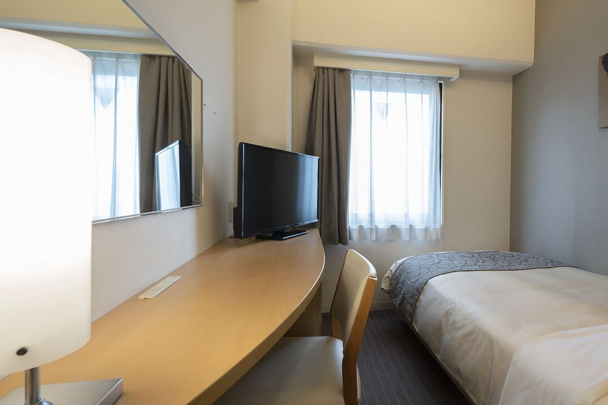 Une chambre d’hôtel avec un lit, un bureau, une chaise, une télévision et une fenêtre avec des rideaux.