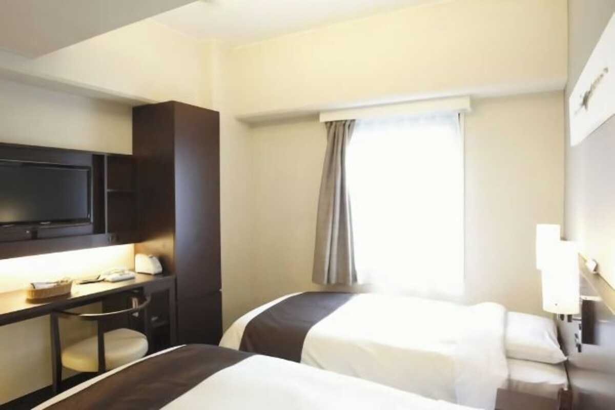 A hotel room with two beds, a desk with a television, and a window with curtains.