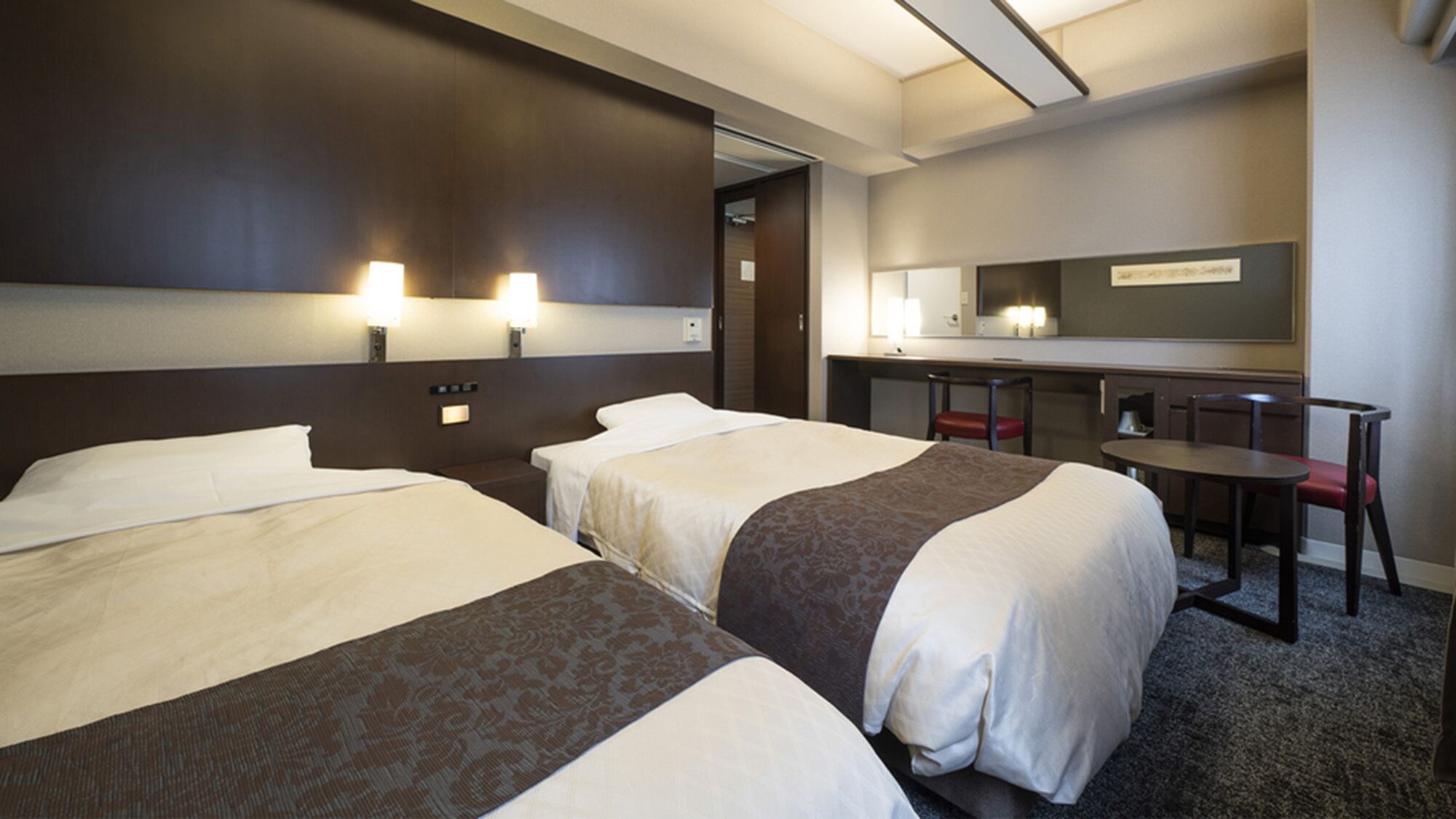 Ein Hotelzimmer mit zwei Betten, einem Schreibtisch, einem Stuhl und einem Spiegel.